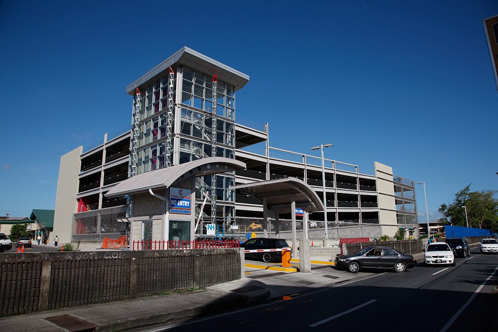 The Chaguanas Main Road outside the mall: the glazed stair tower, the car park deck, buses and traffic passing.